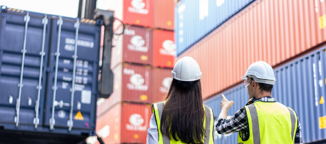 A man and a woman in hard hats and PPE looking at a crane loading cargo.